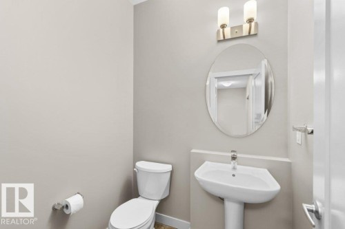Pedestal sink with a polished chrome faucet, oval mirror, and a two-bulb vanity light fixture - 1523 168 Street Sw, Edmonton, AB 