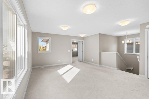 Carpeted open-plan area featuring multiple windows, a ceiling-mounted light fixture, and a staircase with railing - 1523 168 Street Sw, Edmonton, AB 