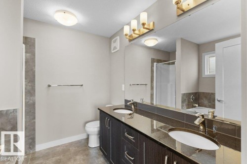 Dual sink vanity with dark wood-finish cabinetry, a large wall-mounted mirror, and a wall-mounted light fixture - 1523 168 Street Sw, Edmonton, AB 