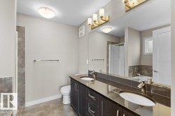 Dual sink vanity with dark wood-finish cabinetry, a large wall-mounted mirror, and a wall-mounted light fixture - 
