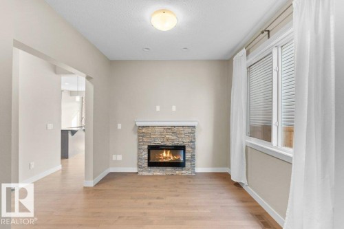 Stone-clad fireplace with an electric insert, wood-finish flooring, and a large window with white blinds - 1523 168 Street Sw, Edmonton, AB 