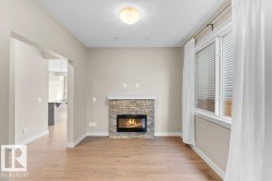 Stone-clad fireplace with an electric insert, wood-finish flooring, and a large window with white blinds - 