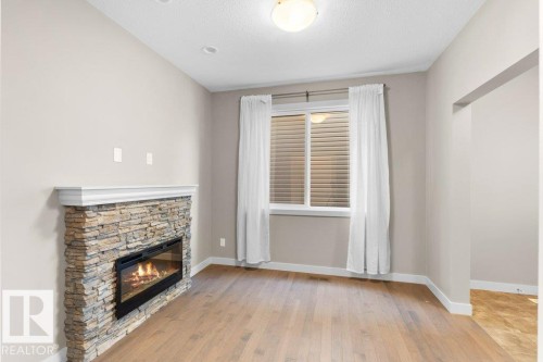Stone-clad fireplace with mantel, recessed lighting, wood-finish flooring, and a large window with blinds - 1523 168 Street Sw, Edmonton, AB 