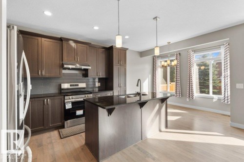 Kitchen featuring wood-finish flooring, dark wood cabinetry, stainless steel appliances, a center island with sink, and recessed lighting - 1523 168 Street Sw, Edmonton, AB 