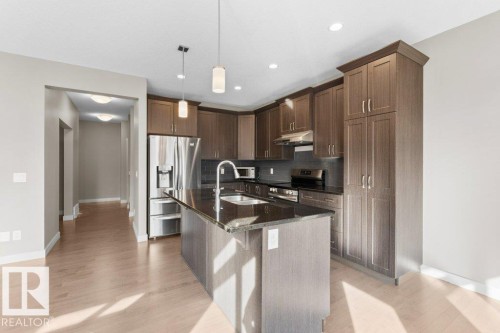Kitchen featuring wood-finish cabinetry, stainless steel appliances, a center island with a sink, pendant lighting, and recessed ceiling lights - 1523 168 Street Sw, Edmonton, AB 