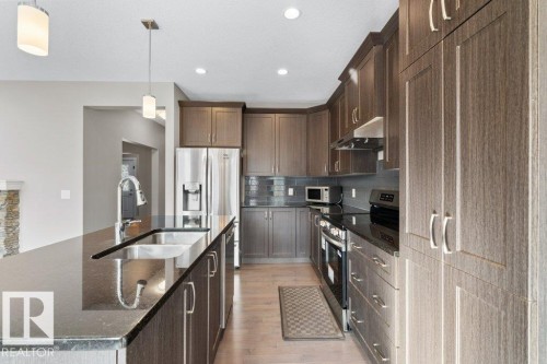 Wood-finish cabinetry, stainless steel appliances, dark countertops, tile backsplash, and light wood-finish flooring - 1523 168 Street Sw, Edmonton, AB 