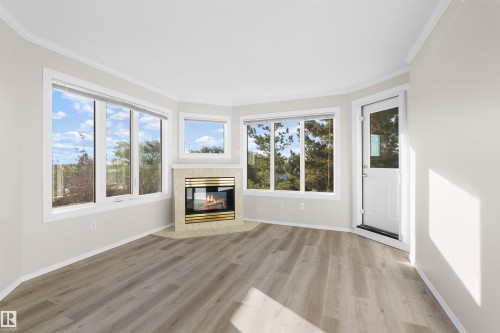 Recessed fireplace with a tiled surround, wood-finish flooring, multiple windows, and crown molding - #408 10610 76 St Nw, Edmonton, AB 