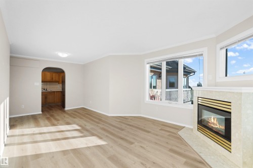 Spacious room featuring wood-finish flooring, a corner fireplace with a tiled surround, multiple windows, and a coved ceiling - #408 10610 76 St Nw, Edmonton, AB 