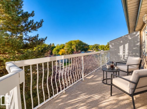 Balcony featuring white railing, textured flooring, and an exterior wall with a light fixture - #408 10610 76 St Nw, Edmonton, AB 
