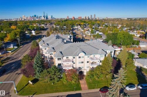 Multi-story building featuring balconies with railings, landscaped grounds, and a paved parking area - #408 10610 76 St Nw, Edmonton, AB 