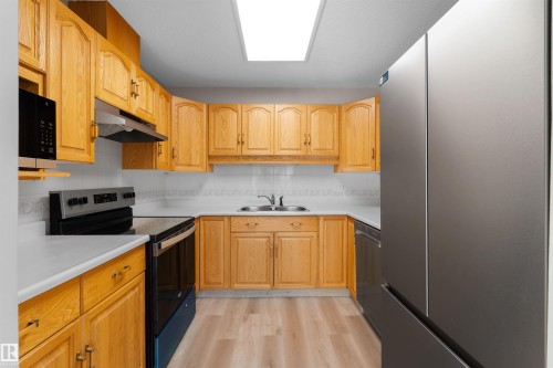 Kitchen featuring wood cabinetry, white countertops, a tile backsplash, and wood-finish flooring - #408 10610 76 St Nw, Edmonton, AB 