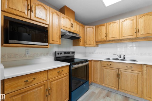 Wood-finish cabinetry, white countertops, white tile backsplash, integrated microwave, and a double basin sink - #408 10610 76 St Nw, Edmonton, AB 