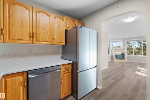 Wood-finish cabinetry with stainless steel appliances, white countertop, and tiled backsplash - #408 10610 76 St Nw, Edmonton, AB 