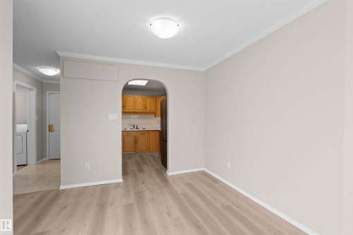 Light-toned wood-finish flooring, neutral wall paint, white crown molding, and an arched doorway - #408 10610 76 St Nw, Edmonton, AB 