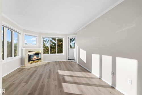 Wood-finish flooring, corner fireplace with a tiled surround, multiple windows, and a white entry door - #408 10610 76 St Nw, Edmonton, AB 