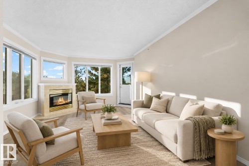 Living area featuring a gas fireplace with a light-toned tile surround and brass accents, wood-finish flooring, and crown molding - #408 10610 76 St Nw, Edmonton, AB 