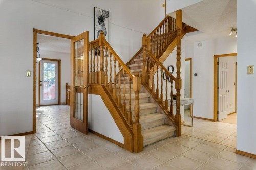 Two-story staircase with wood banisters and carpeted treads, tile flooring throughout the entryway, and a wood-framed glass-paneled door - 507 Burton Close Nw, Edmonton, AB 