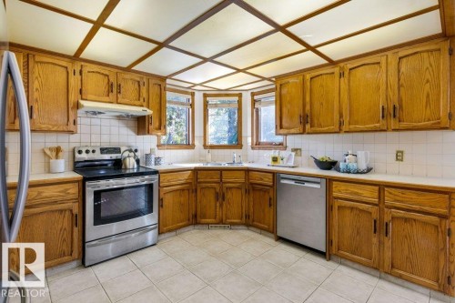 Kitchen featuring wood cabinetry, white tile backsplash, a stainless steel range, and a stainless steel dishwasher - 507 Burton Close Nw, Edmonton, AB 