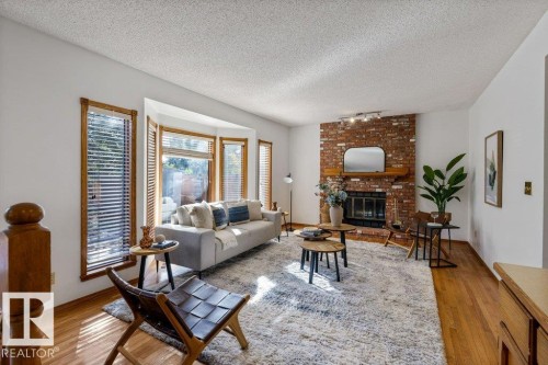 Brick-clad fireplace with wood mantel, bay window with wood trim, wood-finish flooring, and track lighting - 507 Burton Close Nw, Edmonton, AB 