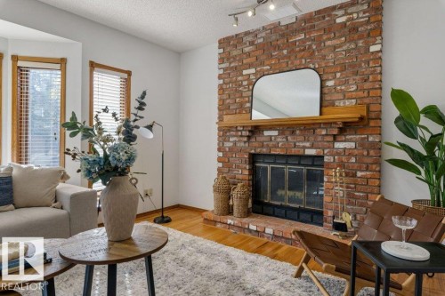 Spacious living room anchored by an exposed brick fireplace with wood mantel and mirror surround, hardwood flooring throughout, and abundant natural light from multi-pane windows - 507 Burton Close Nw, Edmonton, AB 