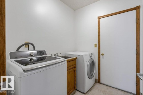 Laundry area featuring tile flooring, wood-finish cabinetry, and a utility sink with a chrome faucet - 507 Burton Close Nw, Edmonton, AB 