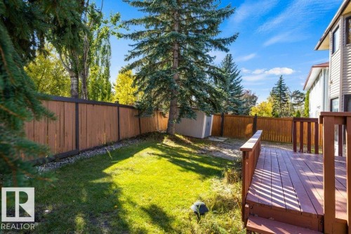 Backyard featuring a wooden privacy fence, mature evergreen trees, a green lawn, and a multi-level wood-finish deck - 507 Burton Close Nw, Edmonton, AB 