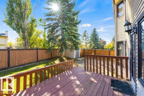 Expansive wood deck with railing, leading to a fenced backyard featuring a grassy area, mature trees, and a storage shed - 507 Burton Close Nw, Edmonton, AB 
