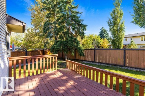Expansive wood deck with a full railing, leading to a lawn area, and bordered by a tall wood fence - 507 Burton Close Nw, Edmonton, AB 