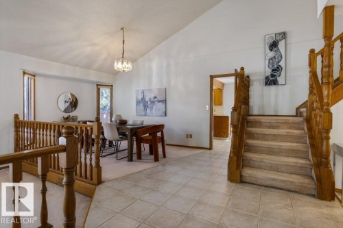 Vaulted ceiling with an elegant chandelier, wood balusters, carpeted staircase, and tiled flooring - 507 Burton Close Nw, Edmonton, AB 