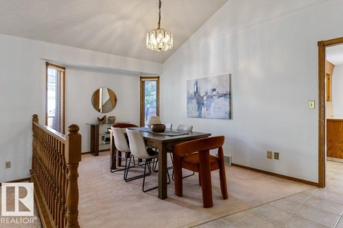 Vaulted ceiling with a decorative chandelier, multiple windows with wood trim, wood railing, and tiled flooring - 507 Burton Close Nw, Edmonton, AB 