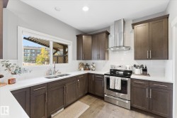 Dark wood-finish cabinetry with silver hardware, white countertops, white subway tile backsplash, stainless steel range with overhead hood, and light wood-finish flooring - 