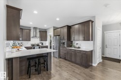 Modern kitchen featuring wood-finish flooring, white countertops, built-in stainless steel appliances, dark wood cabinetry, and a subway tile backsplash - 