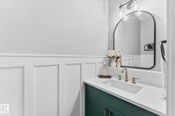 Board and batten wainscoting, a rectangular undermount sink, a white countertop, a green vanity, and a black-framed arched mirror - 