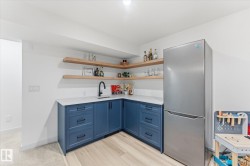 Built-in wet bar featuring blue cabinetry, white countertops, a black gooseneck faucet, light wood-finish flooring, and floating wood shelves - 