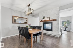 Hardwood-style flooring throughout, featuring a modern fireplace with a white stone surround, a substantial wood mantel, and a multi-bulb chandelier - 