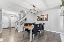 Wood-finish flooring throughout, a modern open-cage chandelier, a white fireplace with stacked stone, and a staircase featuring painted risers and metal balusters - 