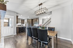 Open-concept living space with wood-finish flooring, a contemporary linear chandelier, and a kitchen featuring dark wood cabinetry and stainless steel appliances - 