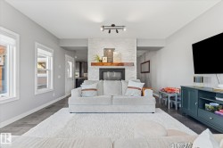 Light-filled living area featuring wood-finish flooring, a white brick fireplace with a wood mantle, and track lighting - 