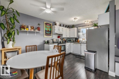 Kitchen dining area featuring dark wood-finish flooring, white cabinetry, stainless steel appliances, and a ceiling fan with integrated lighting - 1040 Lakewood Rd N Nw, Edmonton, AB 