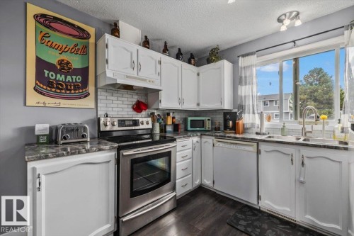 Kitchen featuring white cabinetry, dark countertops, white subway tile backsplash, stainless steel appliances, and wood-finish flooring - 1040 Lakewood Rd N Nw, Edmonton, AB 