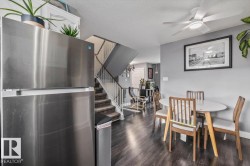 Wood-finish flooring, stainless steel refrigerator, white ceiling fan with integrated lighting, and a staircase with white railings - 