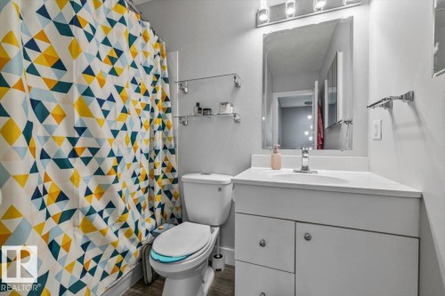 White vanity with an integrated sink and chrome faucet, under-sink cabinetry with polished chrome pulls, mirrored medicine cabinet with integrated lighting, and two glass shelving units - 1040 Lakewood Rd N Nw, Edmonton, AB 