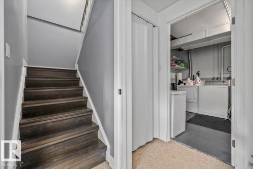 Dark wood-finish staircase with white risers and handrail, adjacent to a utility area with a washer and dryer - 1040 Lakewood Rd N Nw, Edmonton, AB 