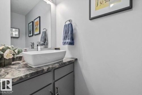 Vessel sink with a chrome faucet, set on a dark patterned countertop, with a vanity featuring gray cabinetry and silver hardware - 1040 Lakewood Rd N Nw, Edmonton, AB 