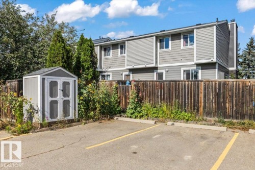 Asphalt parking area with painted space markers, wooden privacy fence, and a gray-painted storage shed - 1040 Lakewood Rd N Nw, Edmonton, AB 