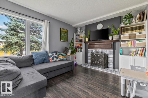Wood-finish flooring, large multi-pane window, and a fireplace with a wood mantle and brick surround - 1040 Lakewood Rd N Nw, Edmonton, AB 