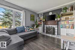 Wood-finish flooring, large multi-pane window, and a fireplace with a wood mantle and brick surround - 
