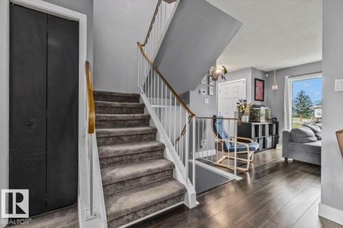 Carpeted staircase with white risers and a wood handrail, dark wood-finish flooring, and a white door with paneling - 1040 Lakewood Rd N Nw, Edmonton, AB 