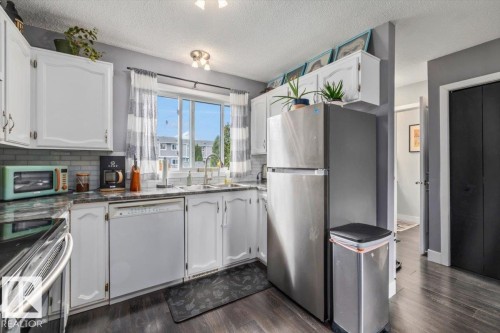 Kitchen featuring white cabinetry, a stainless steel refrigerator, a tile backsplash, and dark countertops - 1040 Lakewood Rd N Nw, Edmonton, AB 