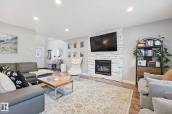 Living area with wood-finish flooring, recessed lighting, and a white stacked stone fireplace - 
